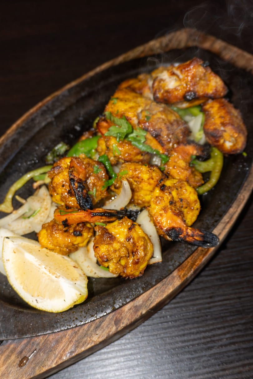 Sizzling platter of grilled shrimp and chicken with onions, peppers, and a lemon wedge.