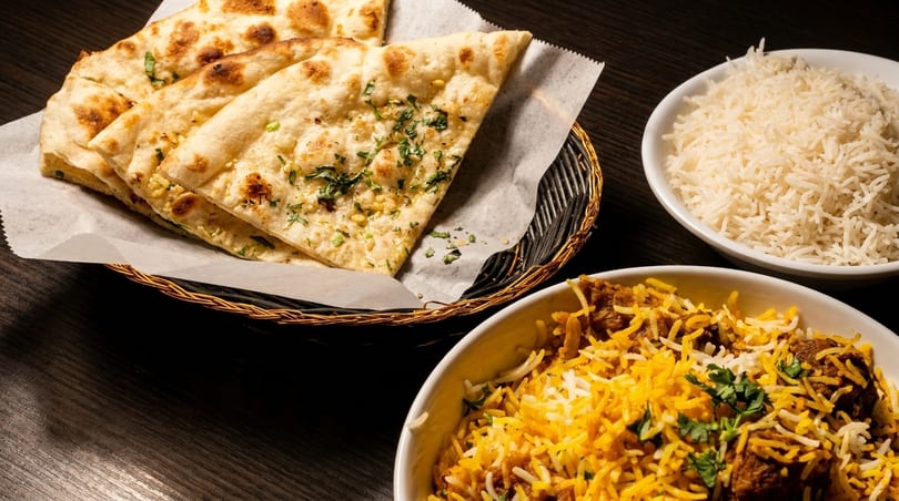 A basket of naan bread, a bowl of white rice, and a bowl of biryani with meat.