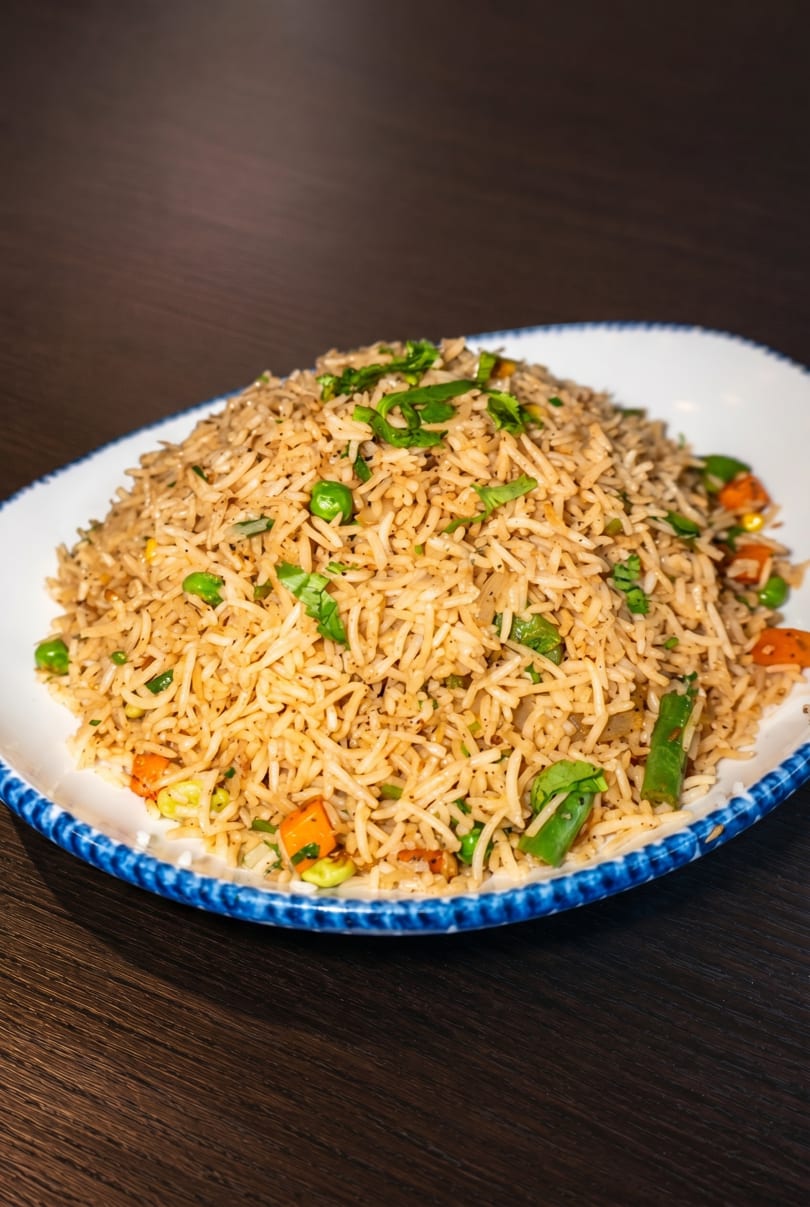 A large serving of vegetable fried rice with peas, carrots, and green onions on a white and blue plate.