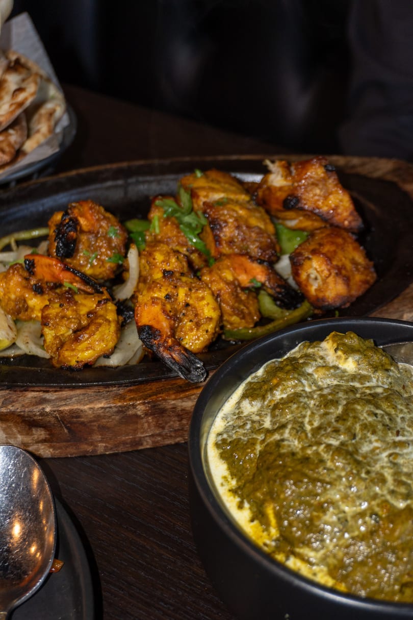 Sizzling platter of chicken and shrimp tikka with a side of creamy green saag.