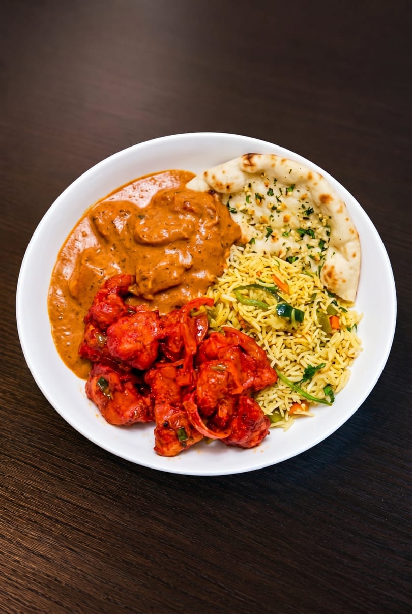 A white bowl filled with butter chicken, chili chicken, vegetable rice, and garlic naan.